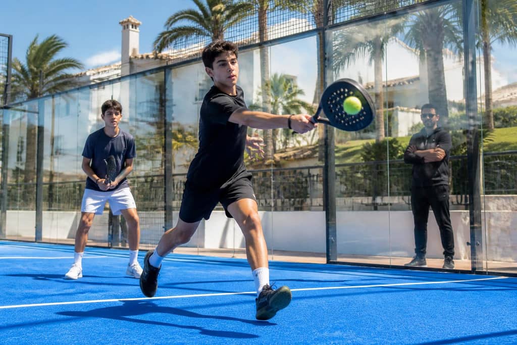 Ungdomar spelar padel på bana med glasväggar